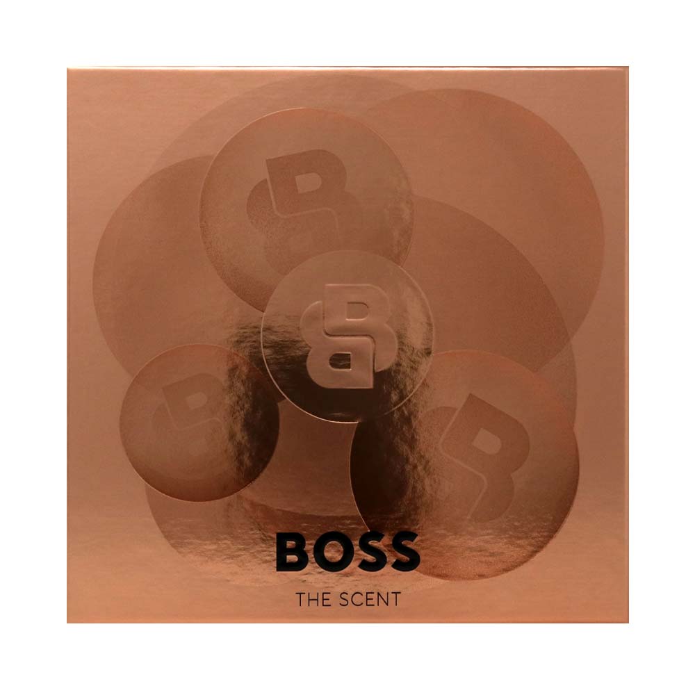 A square metallic rose gold box for BOSS The Scent, featuring a subtle circular floral pattern with the BOSS logo and the text 'BOSS THE SCENT' in black at the bottom.